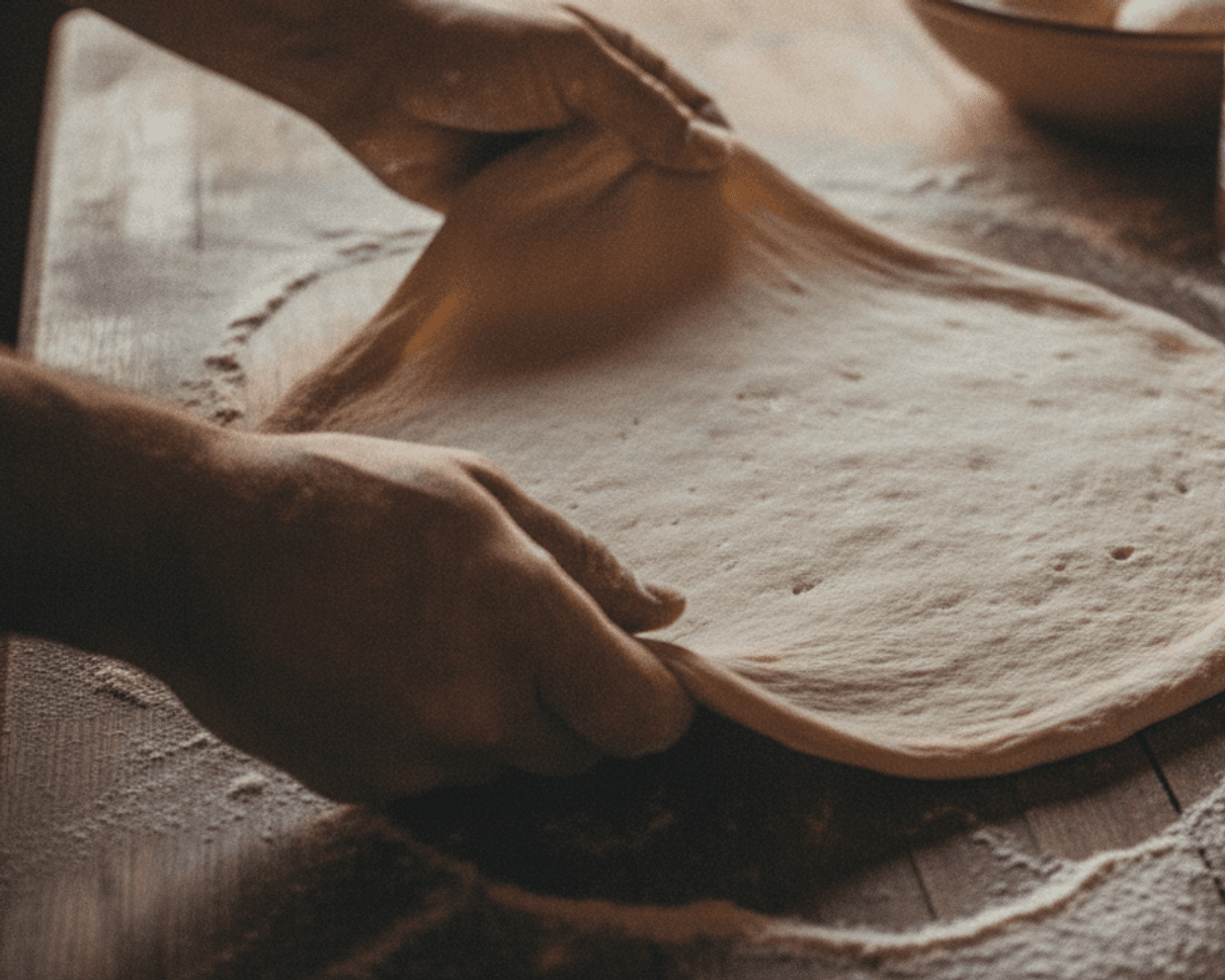 Bemehlte Hände ziehen frischen Pizzateig auf dem Holzbrett aus